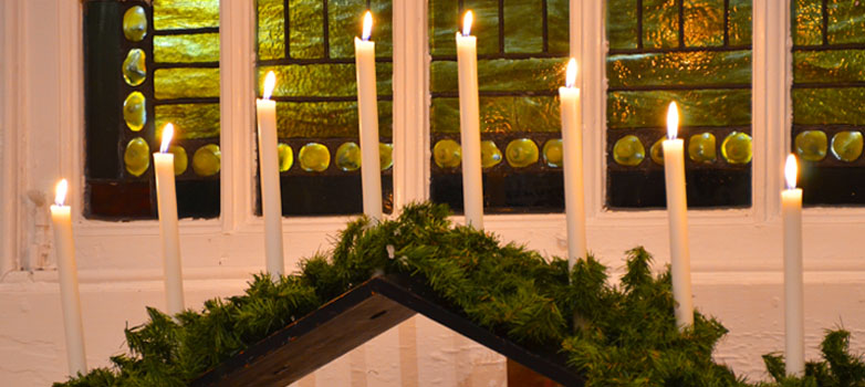 Lit candles in front of a stained glass window.