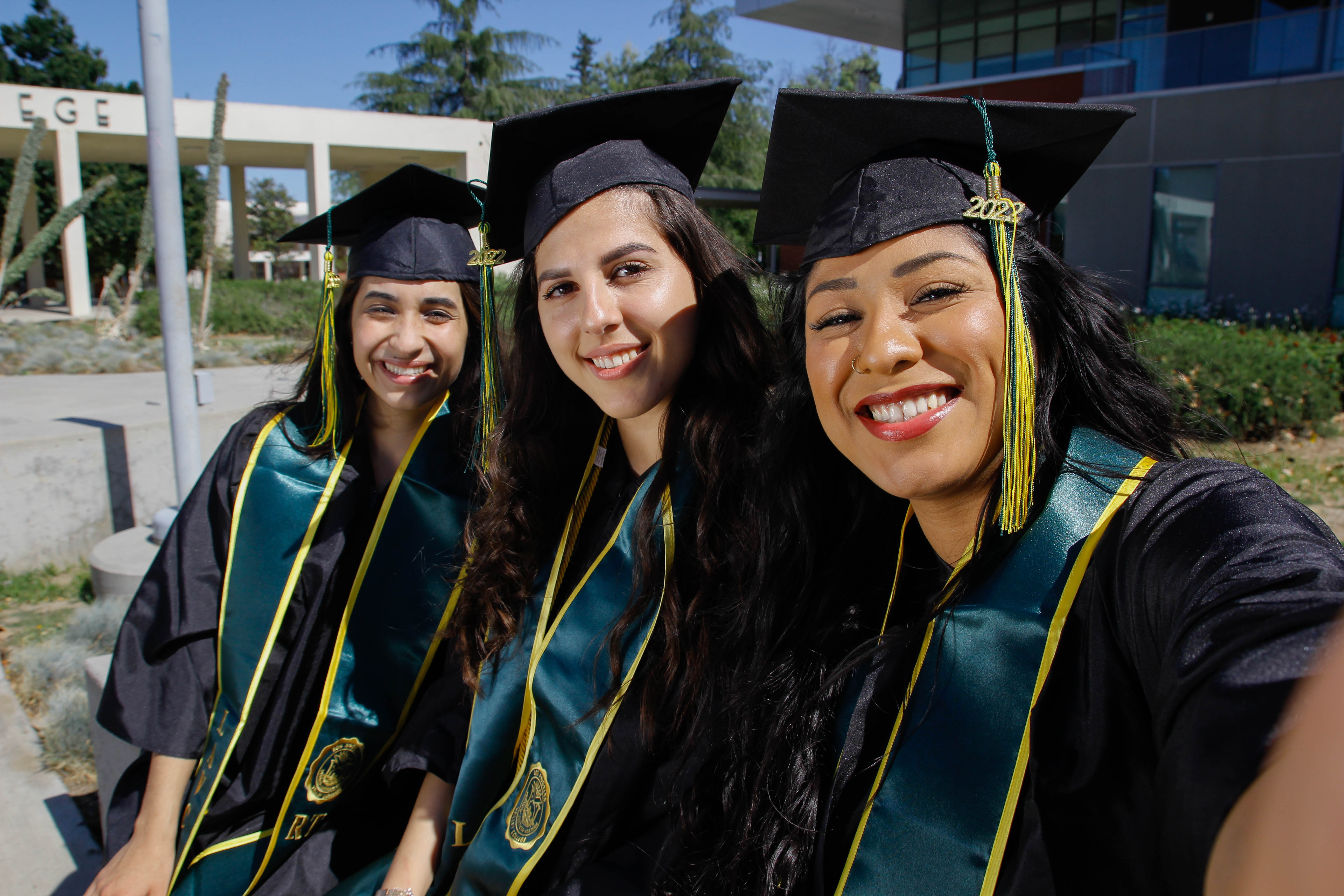 Three smiling grads in caps and gowns outside LAVC