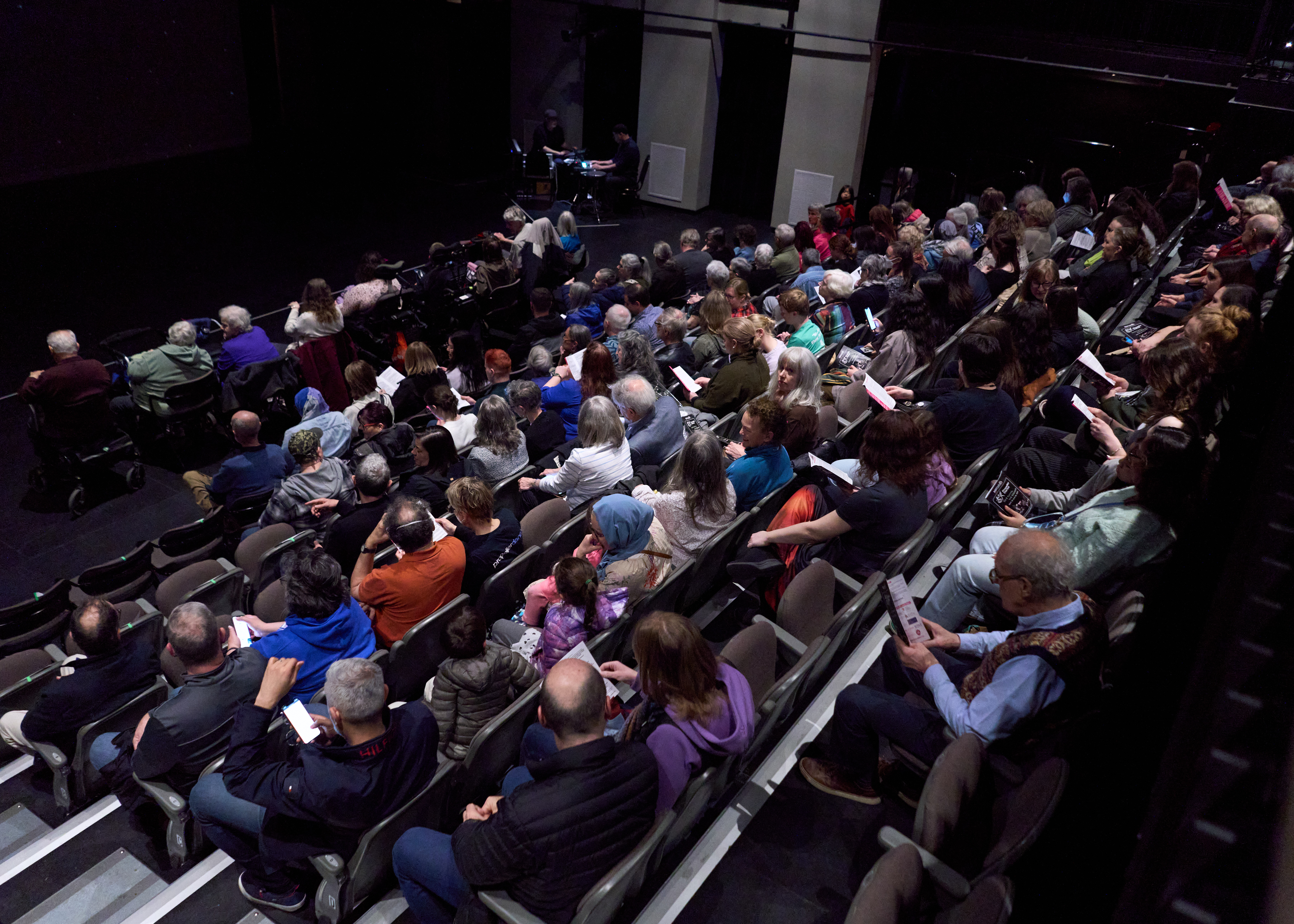 A theatre audience, seen from behind and on an angle, waiting for the show to start