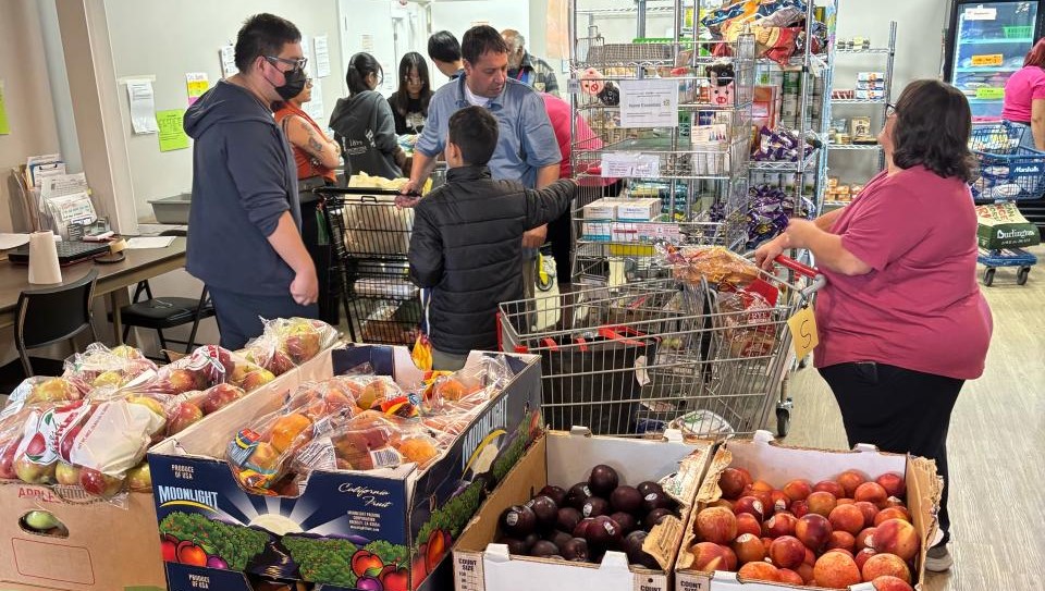 Photo of a Feast of Justice food distribution. Guests choose produce and food for their carts, while volunteers assist. 