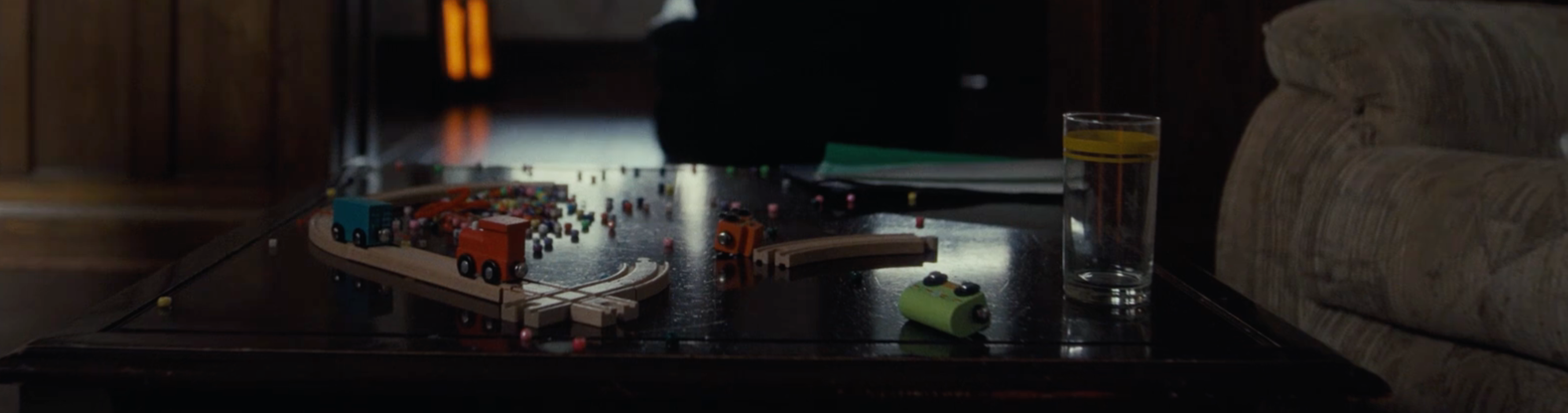 A brown coffee table in a domestic setting, with a broken train track kids toy.