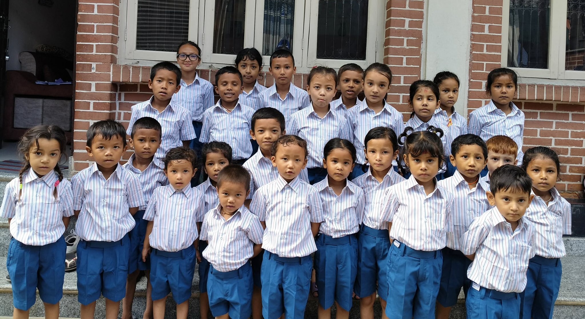 26 Contact Center children in their new uniforms: white button down shirts with blue and red stripes and blue shorts.